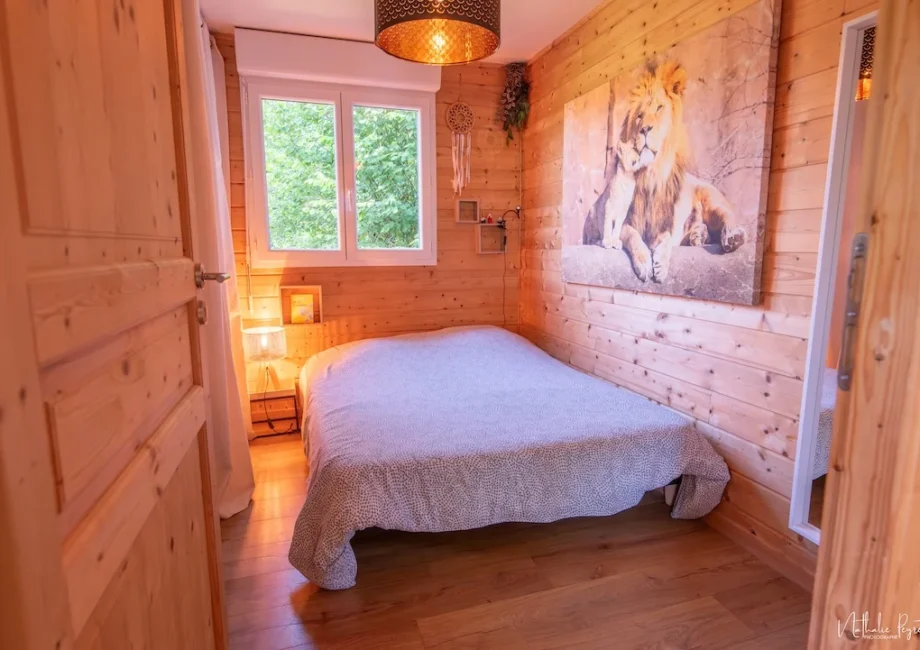 Chambre en bois avec lit double, tableau de lion et lumière douce.
