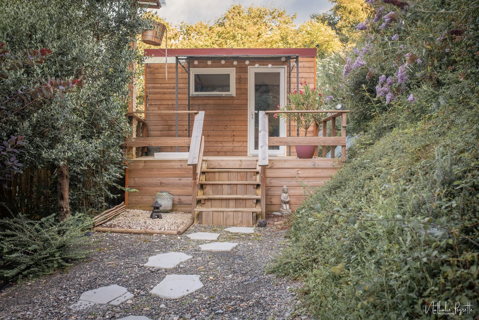 Cabane en bois abritant un sauna infrarouge, entourée de végétation luxuriante avec douche extérieure visible.