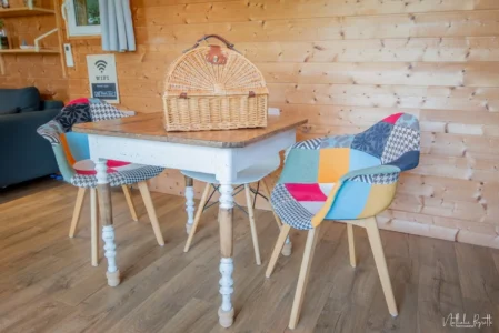Table en bois et chaises patchwork dans le chalet, avec un panier en osier posé dessus.