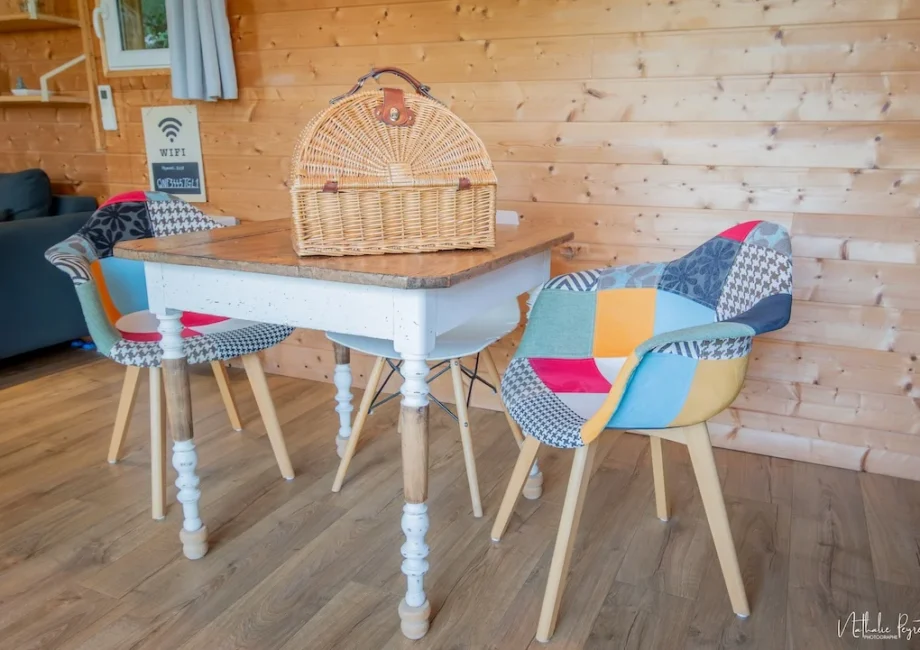 Table en bois et chaises patchwork dans le chalet, avec un panier en osier posé dessus.