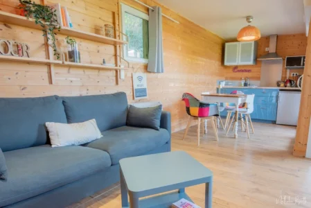 Vue intérieure du chalet Bien-Hêtre, en bois avec canapé, salon et kitchenette en fond.