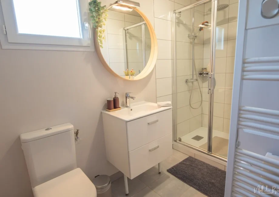 Salle d’eau du chalet avec vasque, miroir rond et douche vitrée.