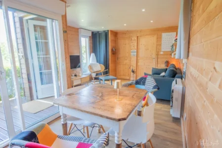 Intérieur lumineux du chalet en bois avec coin salon, table à manger et grandes baies vitrées.