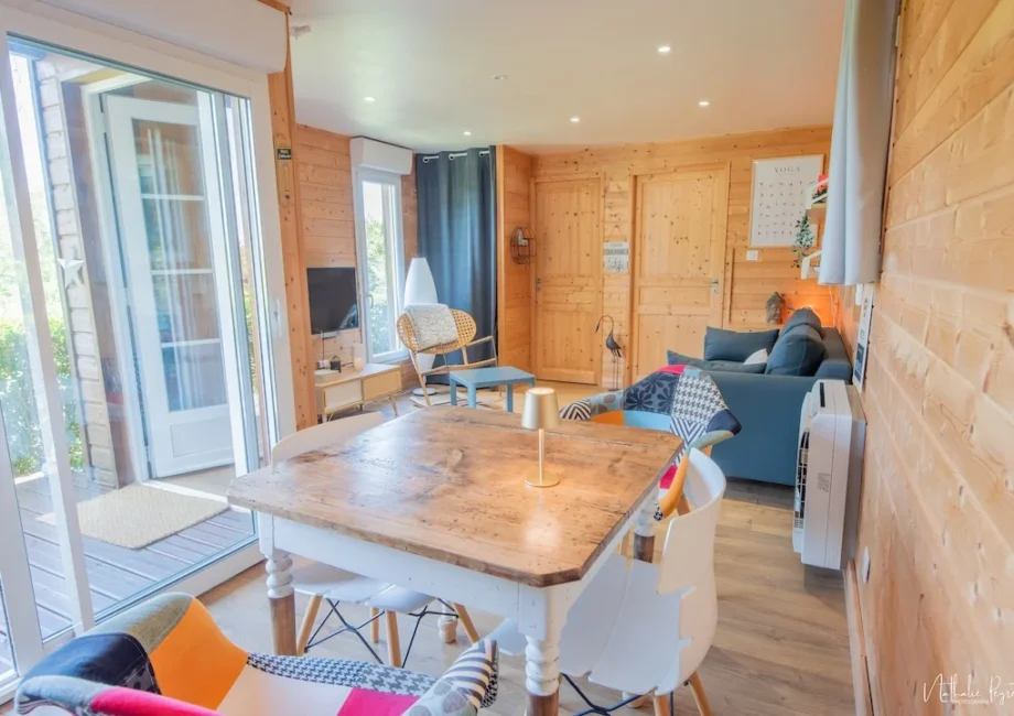 Intérieur lumineux du chalet en bois avec coin salon, table à manger et grandes baies vitrées.