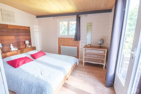 Chambre lumineuse du lodge avec lit double, commode et vue sur la terrasse.