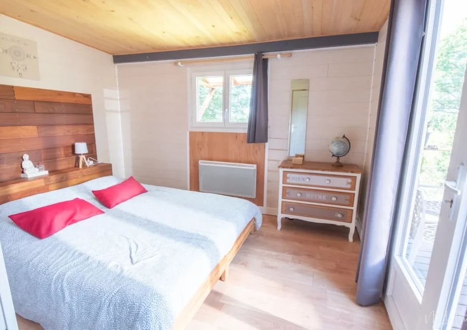 Chambre lumineuse du lodge avec lit double, commode et vue sur la terrasse.