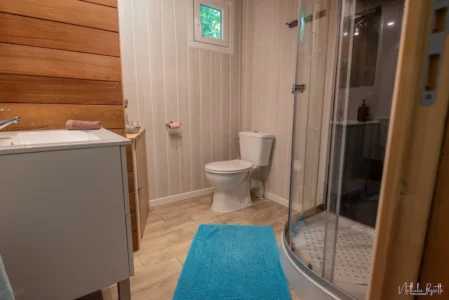 Salle de bain privative du lodge avec douche, toilettes, lavabo et décoration boisée.