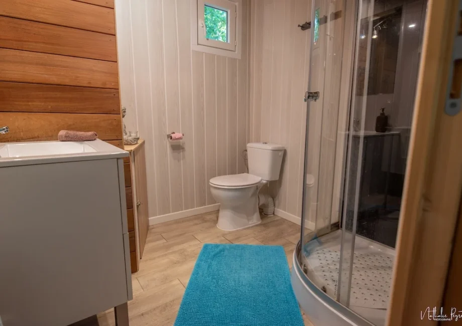 Salle de bain privative du lodge avec douche, toilettes, lavabo et décoration boisée.