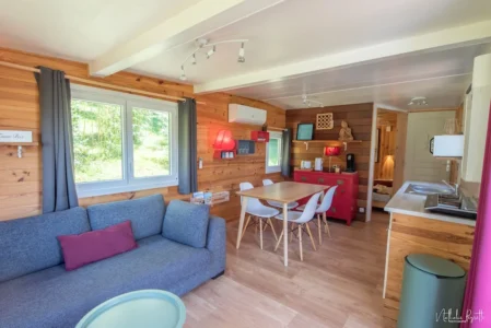 Salon lumineux du lodge avec canapé, coin repas, cuisine équipée et décoration boisée.