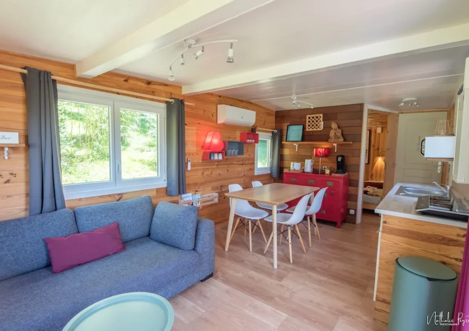 Salon lumineux du lodge avec canapé, coin repas, cuisine équipée et décoration boisée.