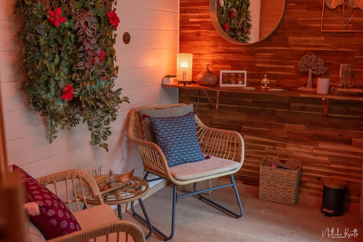 Espace détente cosy avec fauteuils en rotin, coussins, décoration végétale et lumière tamisée dans une salle de repos attenante au sauna.