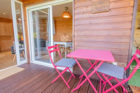 Terrasse en bois du chalet Bien-Hêtre avec table et chaises rose vif, ouverte sur l’intérieur.