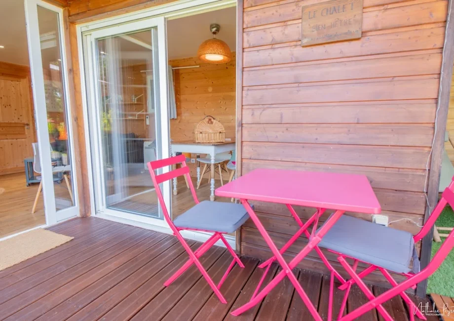 Terrasse en bois du chalet Bien-Hêtre avec table et chaises rose vif, ouverte sur l’intérieur.