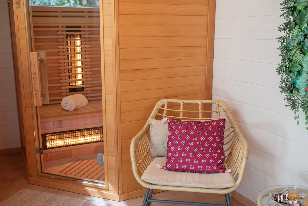Sauna infrarouge en bois avec fauteuil en rotin et coussin, ambiance cocooning.
